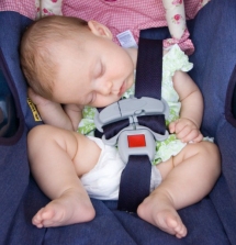 Newborn baby girl slouched over and sound asleep in her car seat.